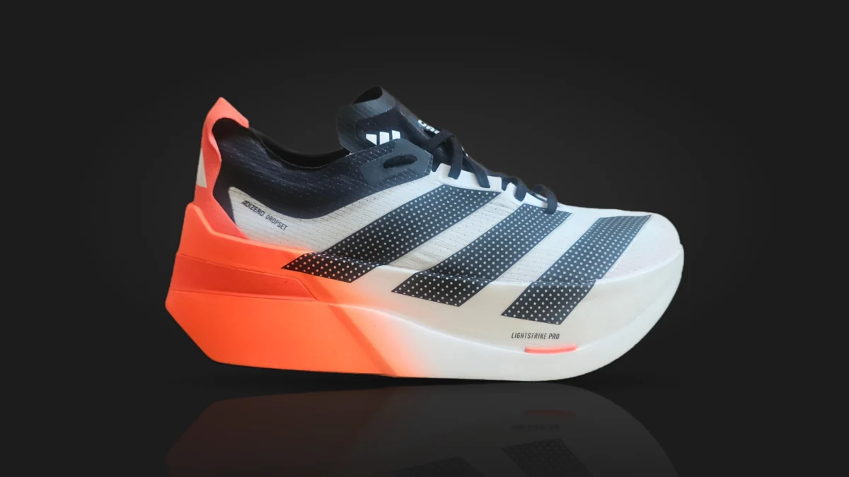 The adidas Adizero Dropset Elite from the side: a white upper with three dotted black stripes, a black collar and laces, and a midsole that fades from orange at the heel to white
