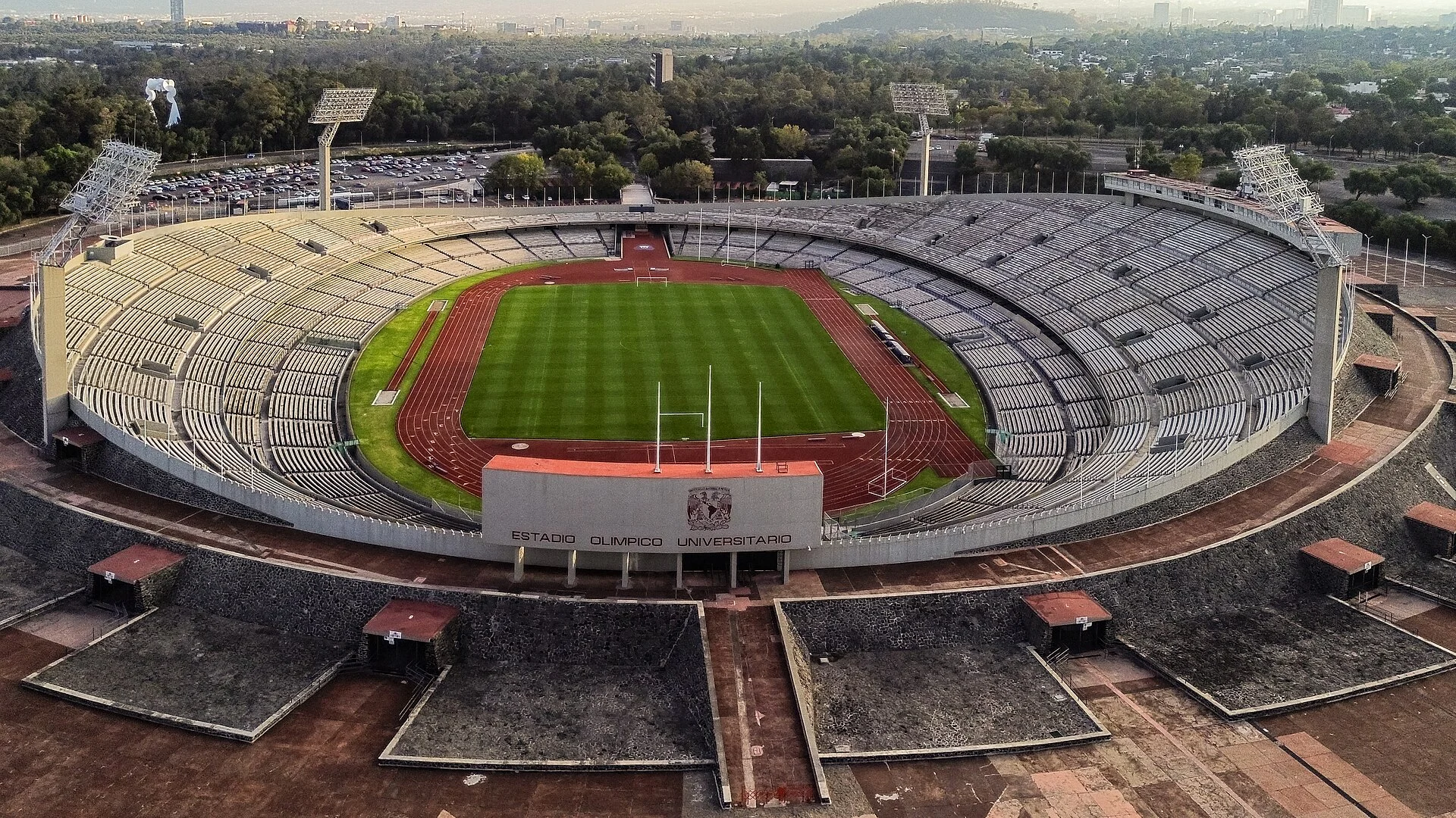 Aerial photograph of the oval Estadio Olímpico Universitario, showing pale terraces, a red athletics track and green pitch in Mexico City.