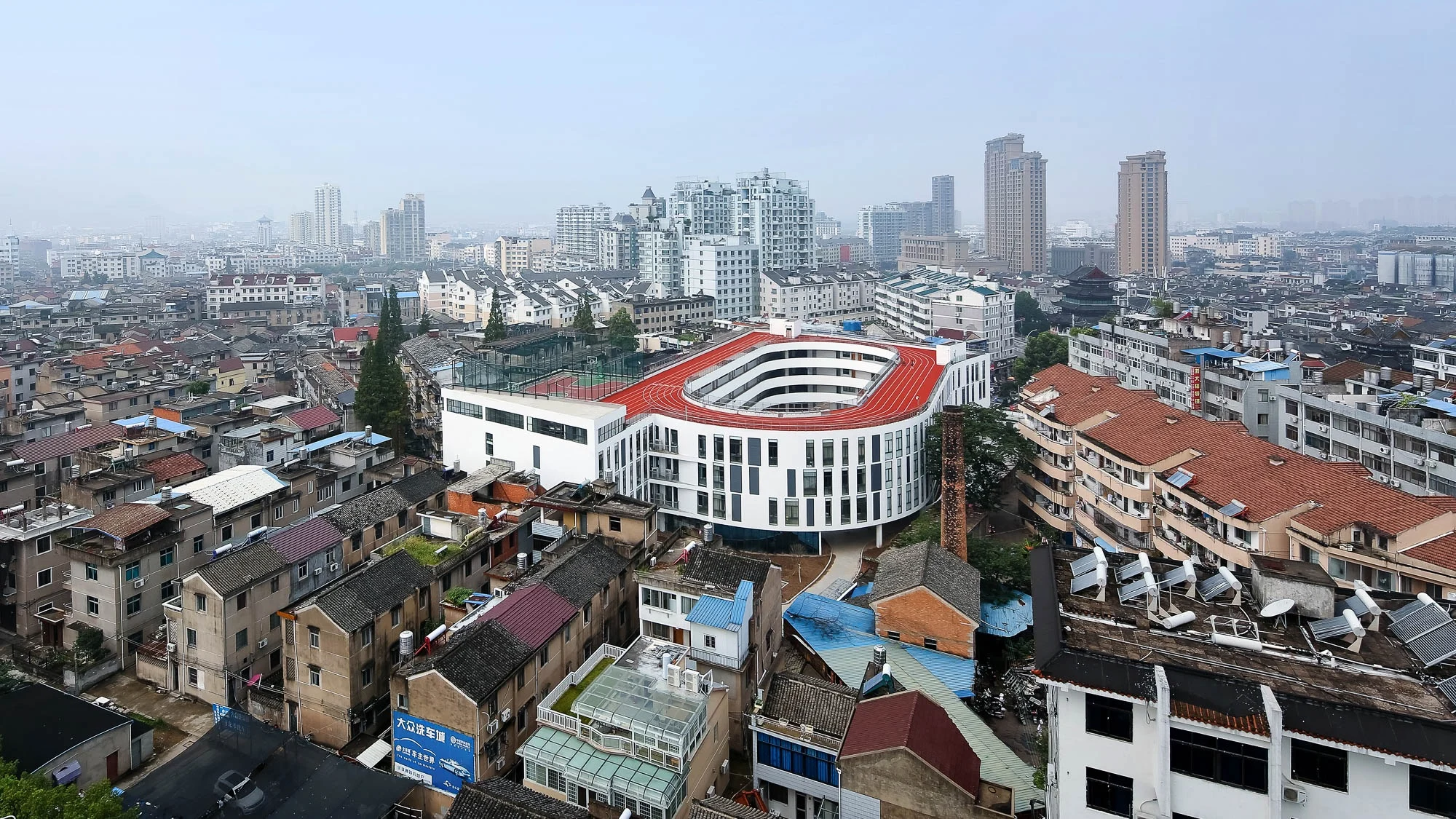The white oval school and its red rooftop track set among tightly packed buildings in Tiantai.